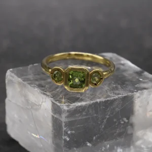 Anillo trilogía de oro amarillo 9k con peridoto central talla cushion y dos peridotos redondos en engaste bisel