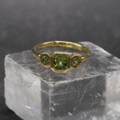 Anillo trilogía de oro amarillo 9k con peridoto central talla cushion y dos peridotos redondos en engaste bisel