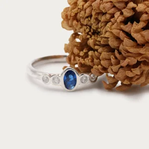 Anillo de oro blanco 18k con zafiro central azul y cuatro diamantes talla brillante G/VS, engaste en bisel