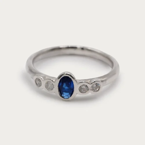 Anillo de oro blanco 18k con zafiro central azul y cuatro diamantes talla brillante G/VS, engaste en bisel
